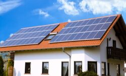 A white house with a red tile roof features large solar panels installed on top, reflecting 2021 solar trends, under a bright blue sky with scattered clouds.
